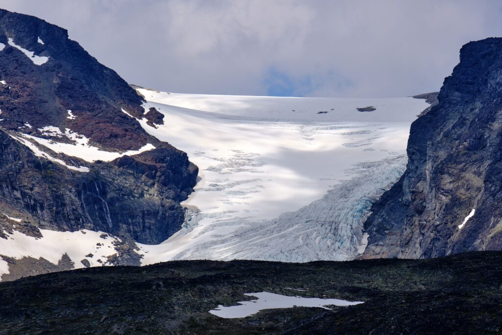 Melting glacier between rugged mountain peaks, illustrating the visible impacts of climate change on Earth's frozen landscapes.