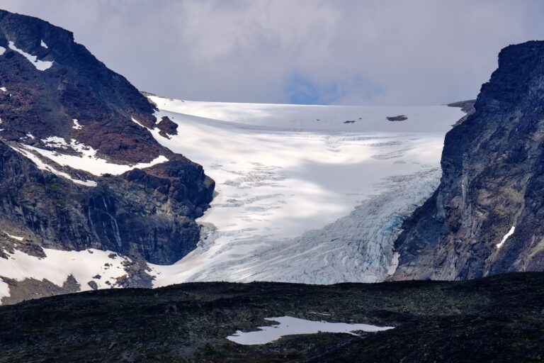 Melting glacier between rugged mountain peaks, illustrating the visible impacts of climate change on Earth's frozen landscapes.