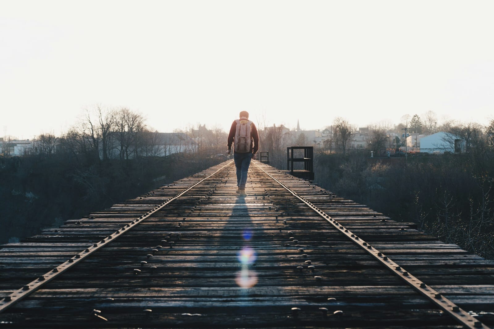 Person walking alone toward sunlight on an old railway bridge