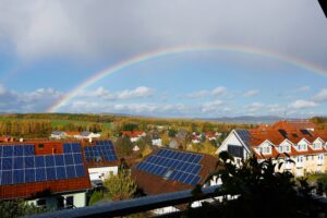 Solar panels on rooftops beneath a rainbow over a green landscape