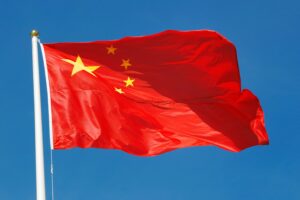 China's red national flag with five golden stars waving against the sky.